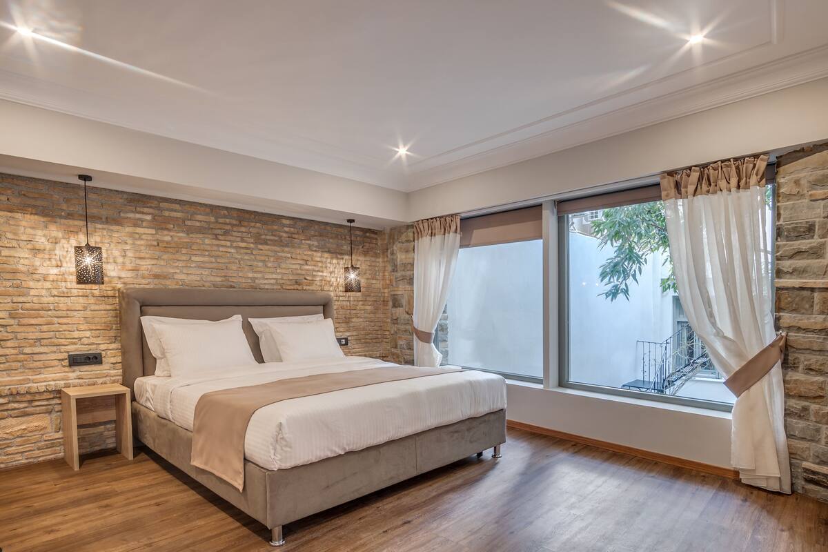 A bedroom with a large bed, stone wall, wooden floor, and a window with curtains.