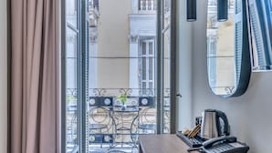Habitación de hotel con balcón, una mesa con sillas, un teléfono y un espejo en la pared.