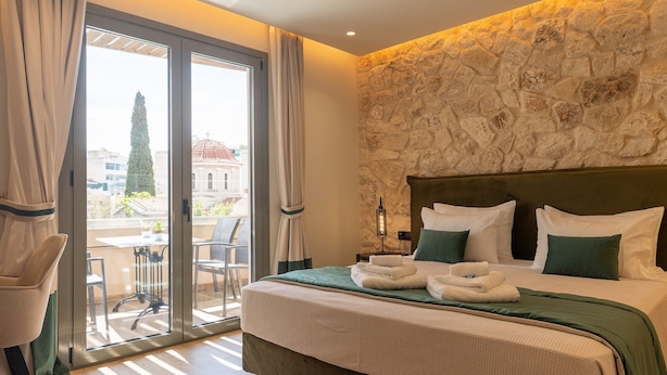 Habitación de hotel con una cama, vistas a la ciudad y un balcón con sillas.