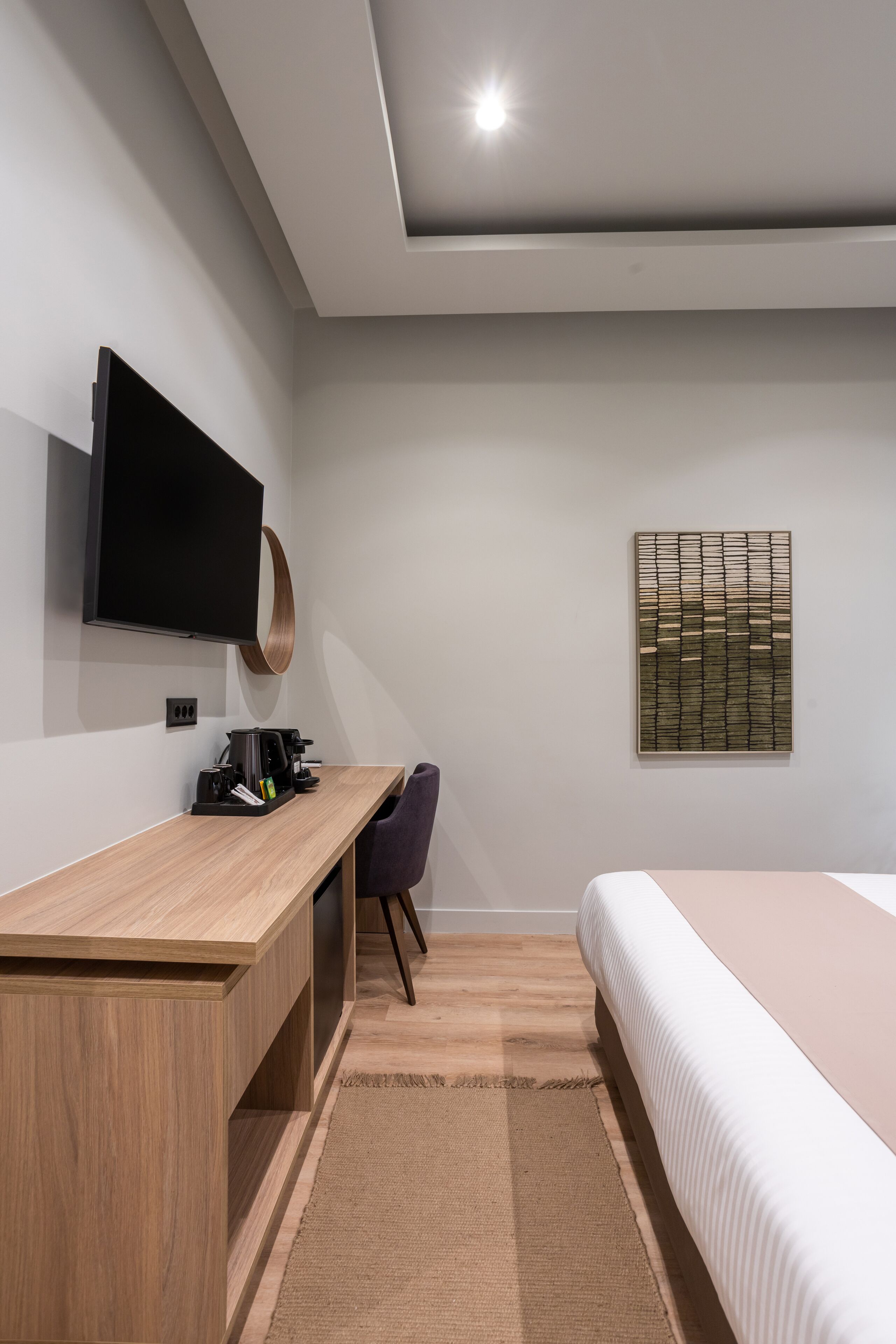 A modern bedroom with a wooden desk, a flat-screen TV, a bed, and a wall-mounted artwork.
