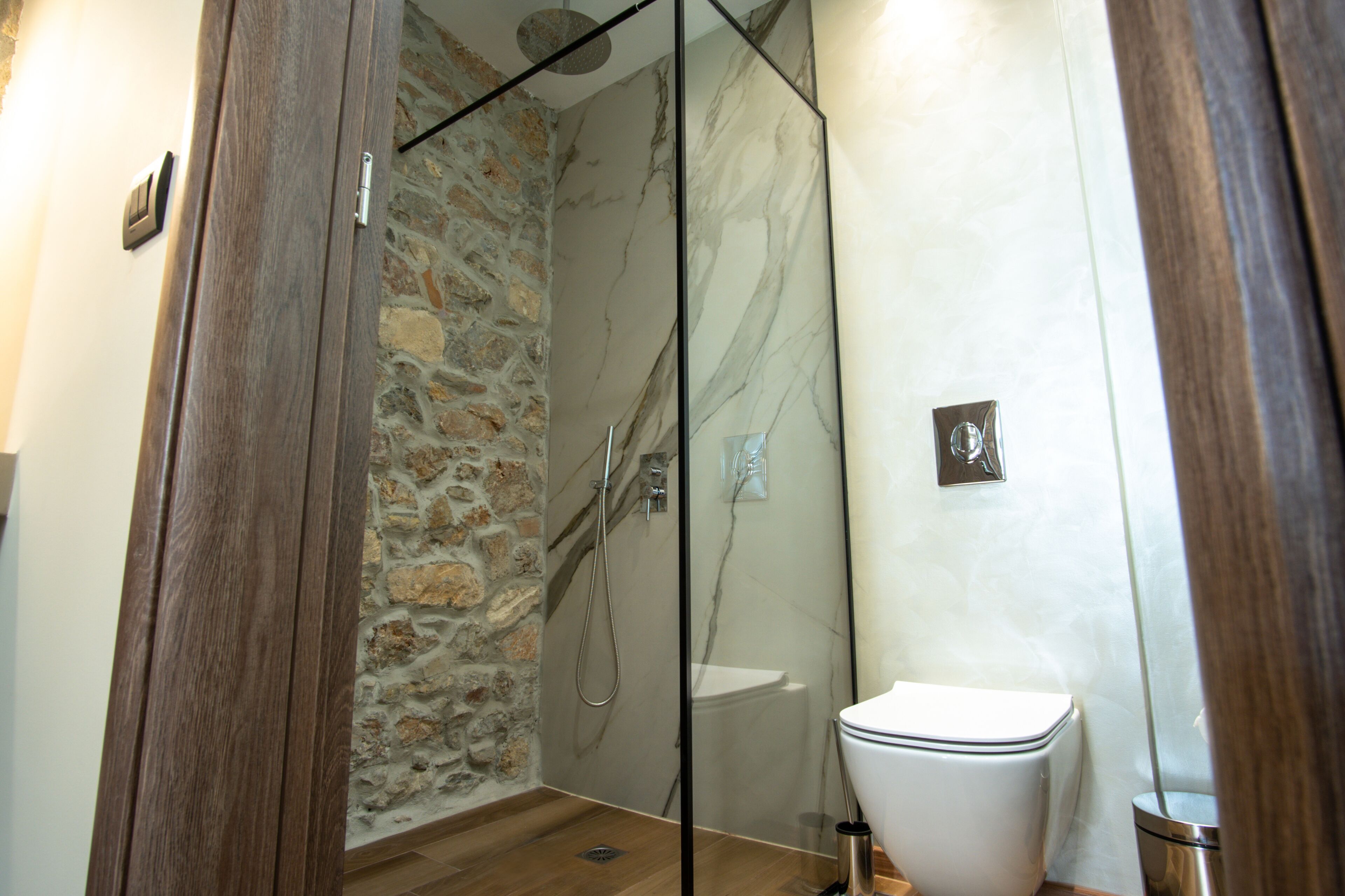 Une salle de bain avec une douche à parois de verre, des toilettes et un mur en pierre.