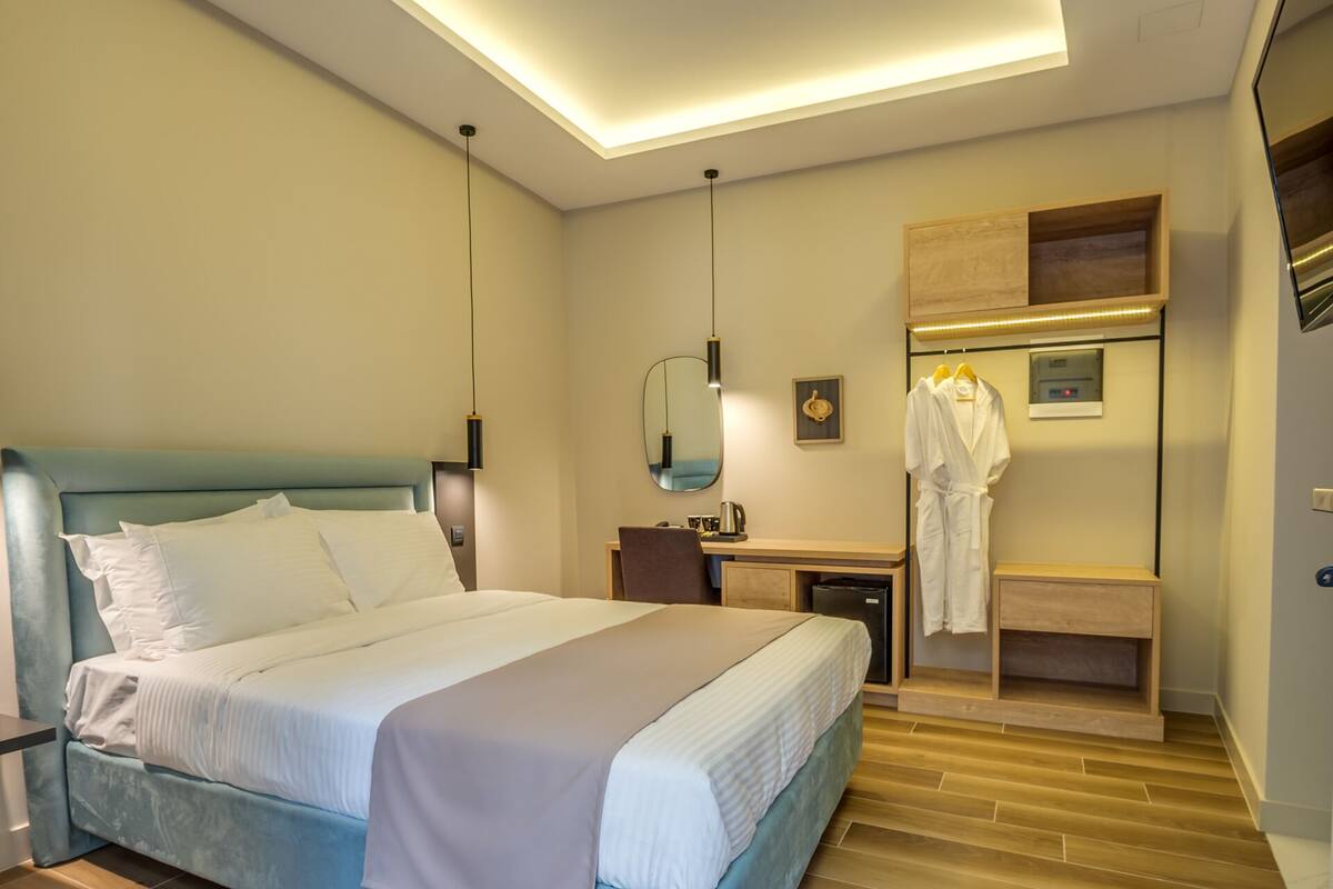 A hotel room with a bed, a desk, a mirror, and a robe hanging on a rack.