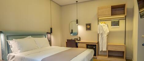 A hotel room with a bed, a desk, a mirror, and a robe hanging on a rack.
