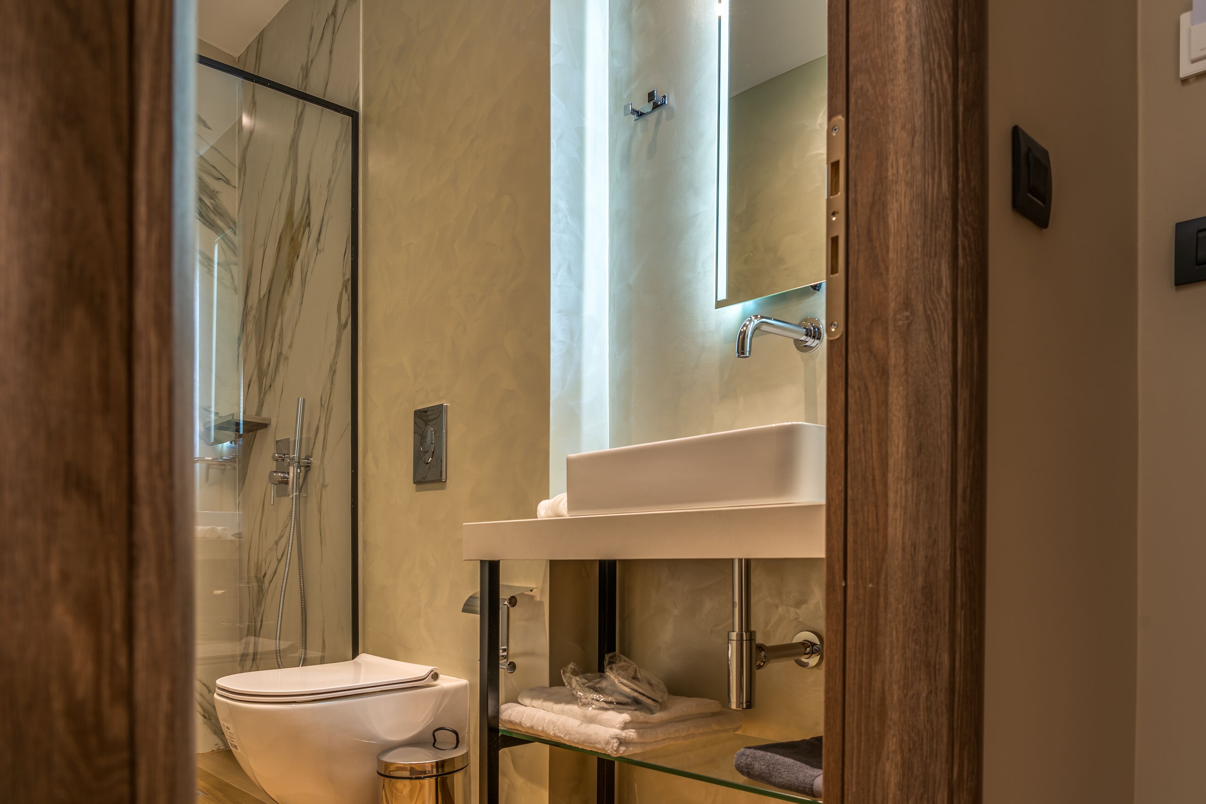 A modern bathroom with a glass shower enclosure, a white toilet, a glass-topped vanity, and a mirror above the sink.