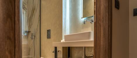A modern bathroom with a glass shower enclosure, a white toilet, a glass-topped vanity, and a mirror above the sink.
