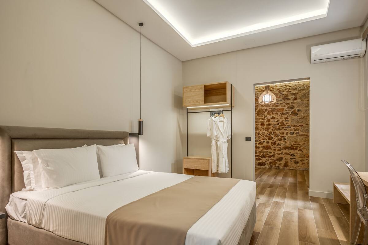 A modern hotel room with a large bed, a wooden wardrobe, a stone wall, and a skylight.