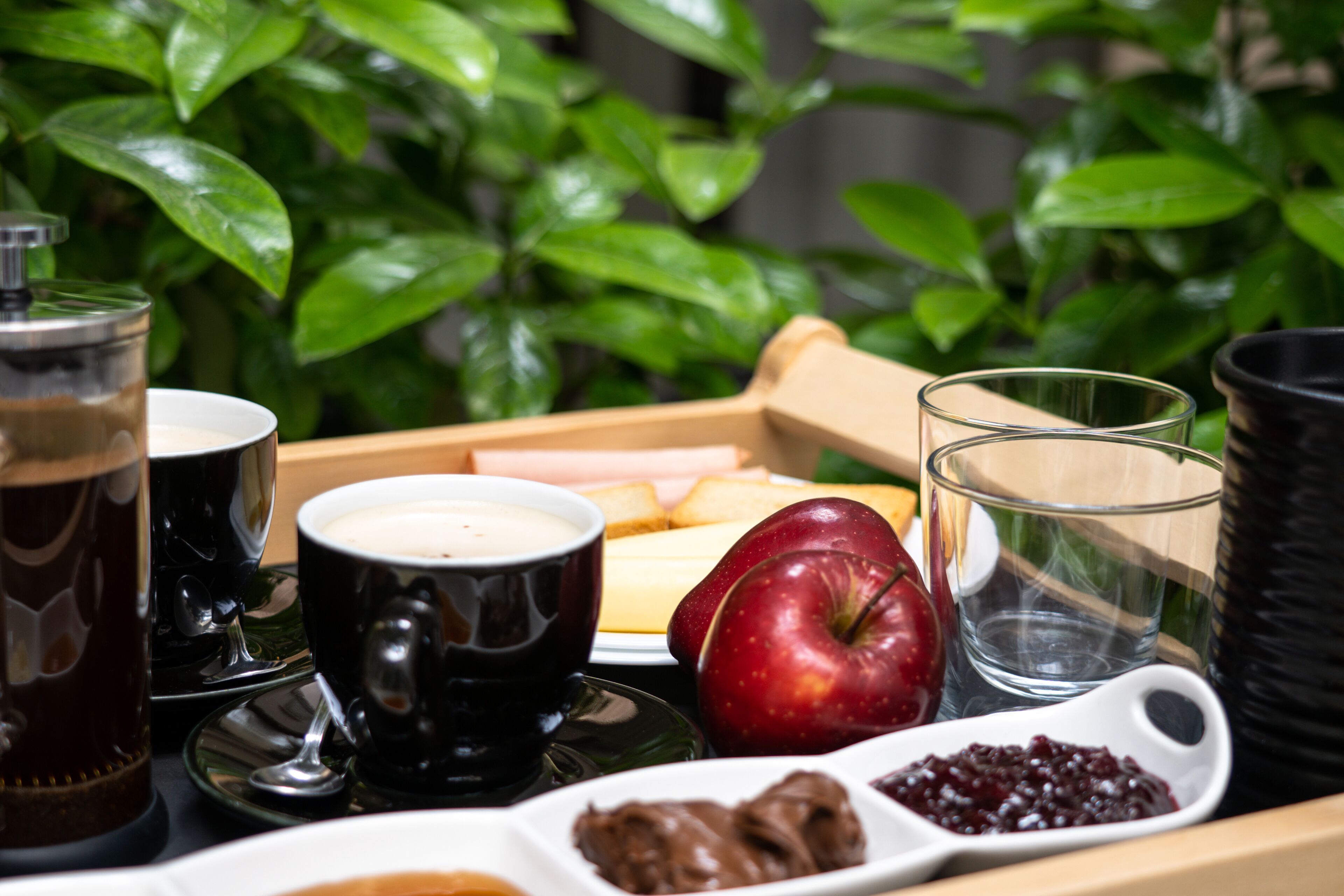 Un vassoio con cibi e bevande, tra cui una mela rossa, crema spalmabile al cioccolato e un bicchiere d'acqua.
