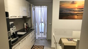 A compact kitchen with a coffee machine, a dining area with a table and chairs, and a view of the sea through a window. - Two steps from the sea and four from the historic center "Donizetti House" (Catania)