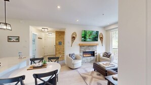 A modern living room with a fireplace, a dining area, and a kitchen. - The Crowe's Nest @ Peaks West (Sun Peaks)