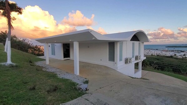A modern white house with a curved roof, a covered porch, and a view of the sea and boats in the background. - Ocean View Sunset (Fajardo)