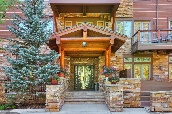 A two-story log cabin with a stone facade, a wooden porch, and a balcony. - Luxury Ski in Ski out Condo/Pool and Hot Tub Access/Private Patio (Keystone)