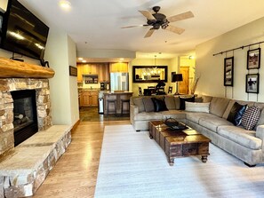 A spacious living room with a stone fireplace, a large sectional sofa, and a wooden coffee table.