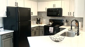 Una cocina moderna con armarios blancos, un refrigerador negro, un microondas y un lavamanos de acero inoxidable.