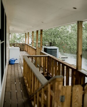 A wooden deck with a railing, a white air conditioning unit, and a blue watering can. - The 1st Camp You'll Want to Stay At! Private Boat Launch & Plenty of Outdoor Fun (Bay St. Louis)