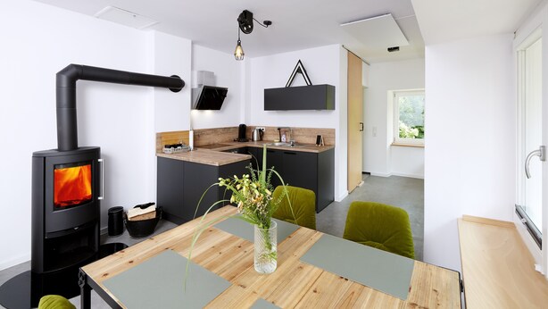 Una cucina moderna con stufa a legna, un tavolo da pranzo con un vaso di fiori e vista sull'esterno.