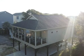 A house with a covered porch, a car parked underneath, and a view of neighboring houses. - Beautiful Beach Home -3 min walk to beach -with golf cart option (Myrtle Beach)