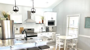 A modern kitchen with stainless steel appliances, white cabinetry, and a central island with bar stools. - Beautiful Beach Home -3 min walk to beach -with golf cart option (Myrtle Beach)