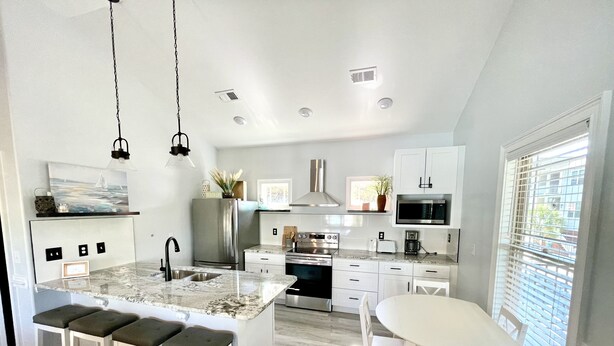 A modern kitchen with a central island, white cabinetry, stainless steel appliances, and a dining area with a round table and chairs. - Beautiful Beach Home -3 min walk to beach -with golf cart option (Myrtle Beach)
