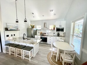 Une cuisine moderne dotée d’un îlot central, de meubles blancs, d’appareils électroménagers en acier inoxydable et d’un coin repas avec une table ronde et des chaises.