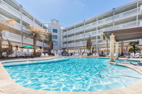 Guests can enjoy a refreshing swim in the central pool surrounded by lounge chairs and umbrellas.