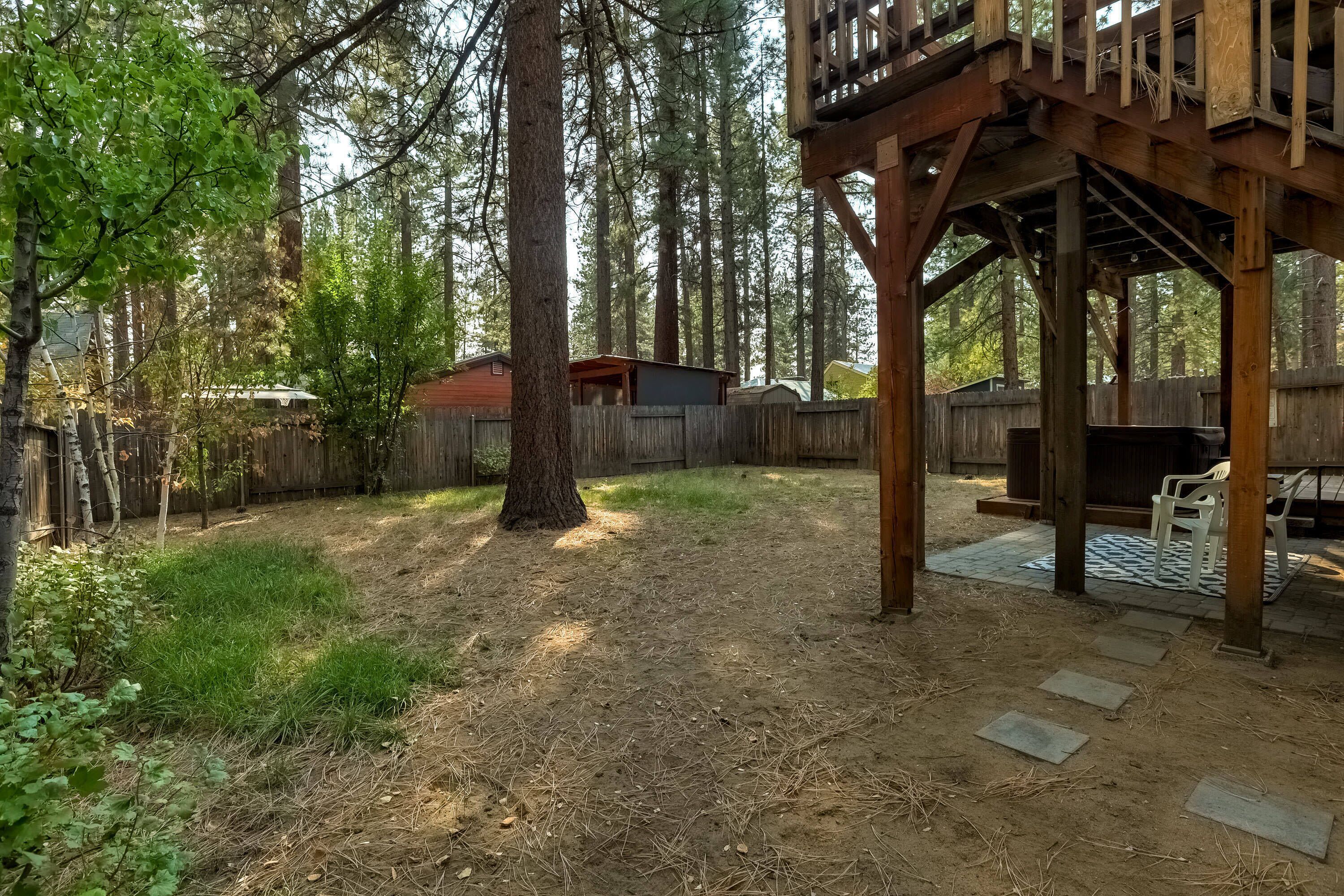 A wooden deck with a rustic wooden fence, a small shed, and a grassy yard surrounded by tall trees.