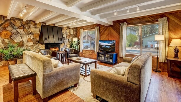A cozy living room with a stone wall, wooden ceiling beams, a fireplace, and a television. - Paloma Place  Hot Tub | Game Room | Pool Table (South Lake Tahoe)