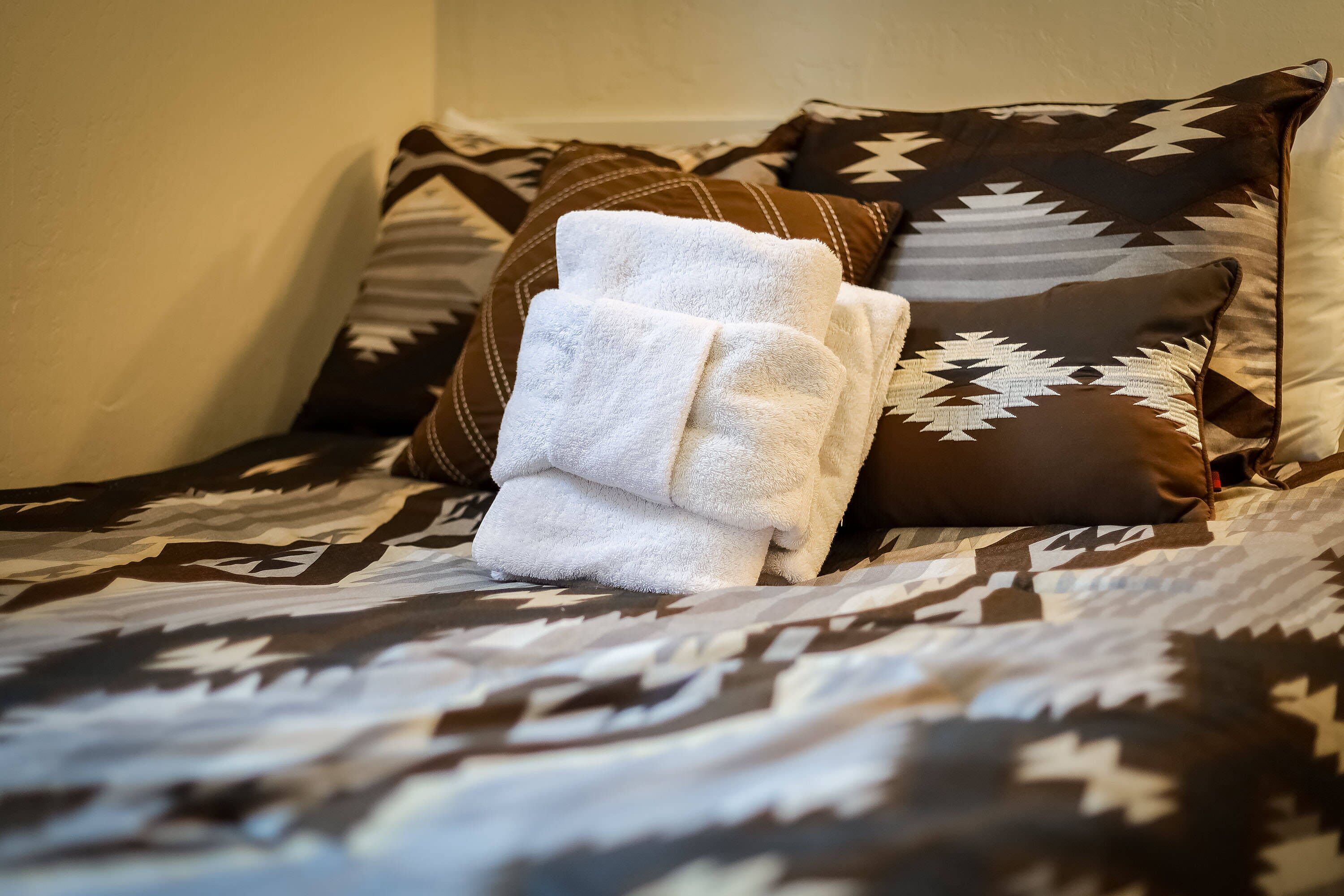 A bed with patterned bedding and a stack of white towels.