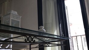 Una habitación con una mesa de vidrio, una silla blanca y vistas a un edificio a través de una ventana con cortinas.