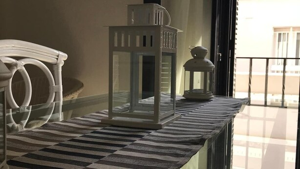 Comedor con mesa de vidrio, mantel a rayas y sillas blancas.