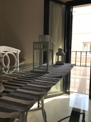 Comedor con mesa de vidrio, mantel a rayas y sillas blancas.