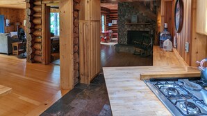 L’intérieur d’un chalet rustique est agrémenté d’une cheminée en pierre, de poutres en bois et d’un coin cuisine avec une cuisinière à gaz.