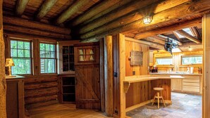 L’intérieur d’un chalet rustique, avec un revêtement mural en bois, un coin cuisine et un espace repas.