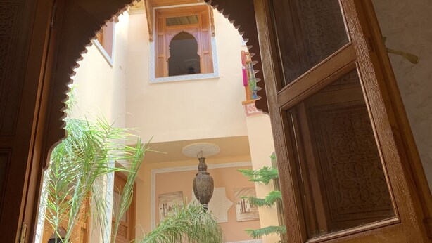 An open wooden door with intricate carvings, leading to a room with a high ceiling, a decorative vase, and a potted plant. - RIADJENANADAM Marrakesh  (Marrakech)