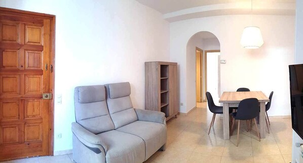 A living room with a sofa, a dining table with chairs, and a bookshelf.