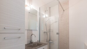A modern bathroom with a glass-enclosed shower, a sink with a mirror above it, and a tiled wall with a brick pattern. - LE PANORAMIQUE - Face mer - Wifi (Pornichet)