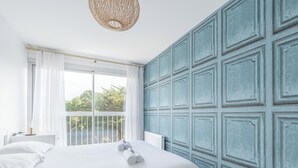 A bedroom with a large bed, a window with curtains, a wall with paneling, and a hanging light fixture. - LE PANORAMIQUE - Face mer - Wifi (Pornichet)
