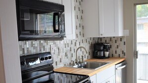 A modern kitchen with white cabinets, a black stove, a microwave, and a wooden countertop. - Feel at Home at this central and spacious 1 bedroom condo (Dallas)