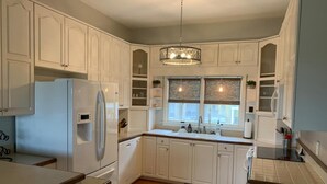 A kitchen with white cabinets, a refrigerator, a sink, and a window with blinds.