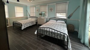 A bedroom with two beds, a dresser, a vanity, and a ceiling fan.