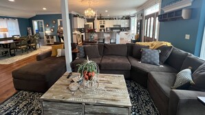 A spacious living room with a large sectional sofa, a wooden coffee table, and a dining area with a table and chairs.