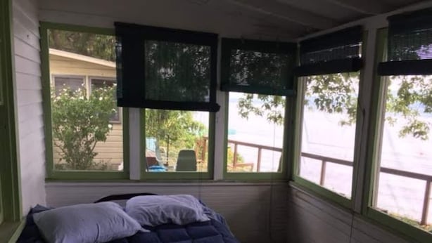 Une petite pièce fermée, avec un lit, une fenêtre munie de stores et une vue sur l’extérieur.