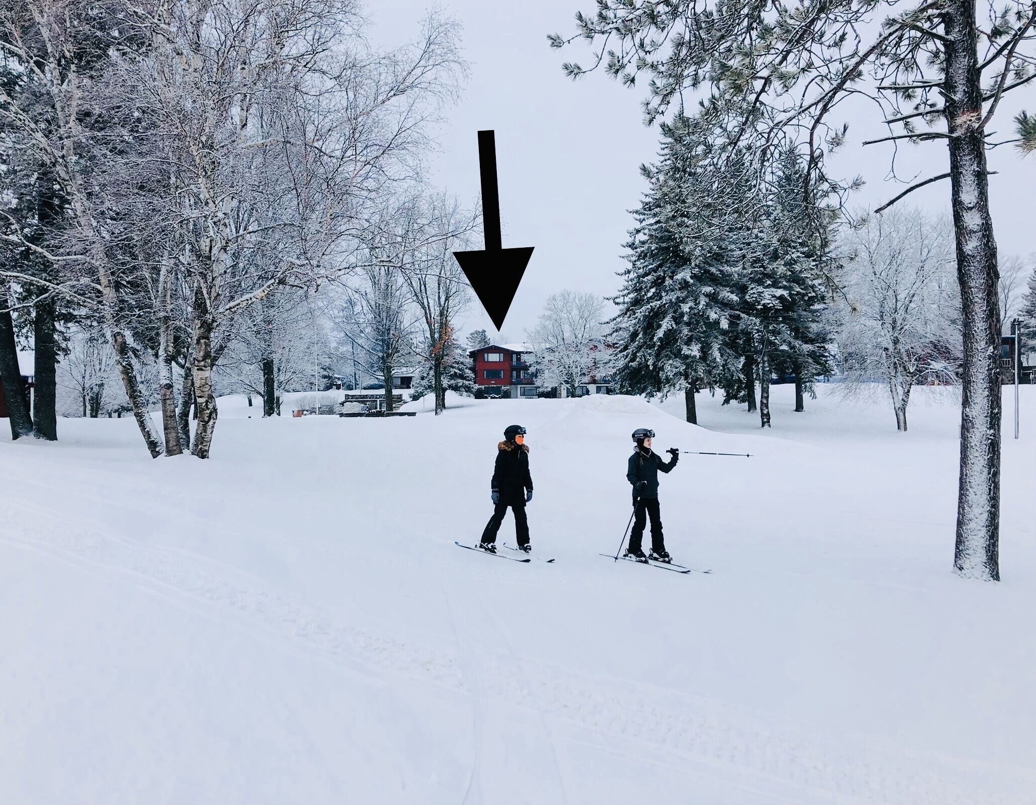 Un paysage enneigé avec deux skieurs et un bâtiment rouge en arrière-plan.