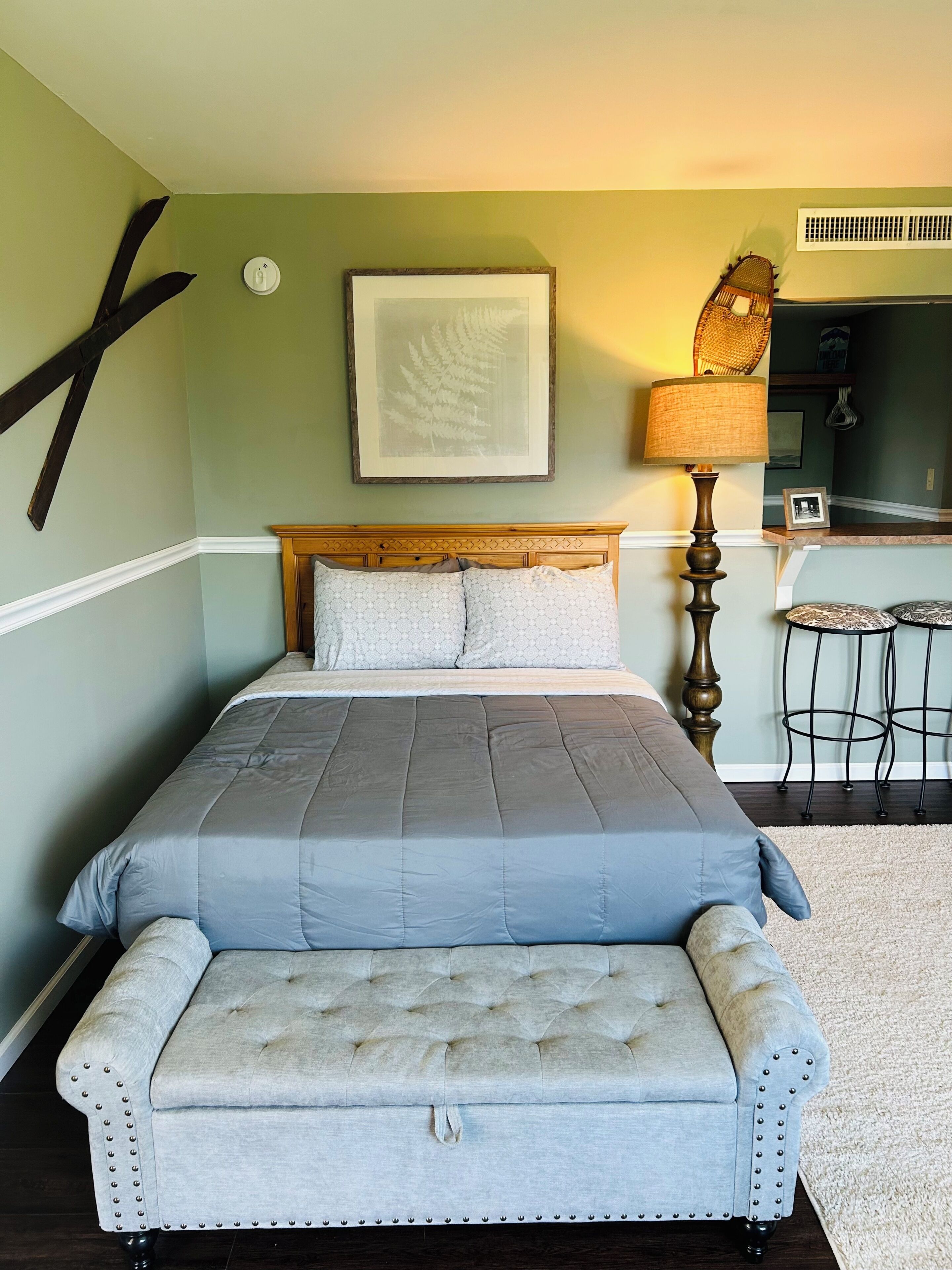 Een slaapkamer met een bed, een bedlampje en een lijst met een afbeelding aan de muur.