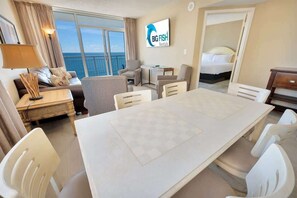 Una habitación de hotel moderna con una gran mesa de comedor, asientos cómodos, una cama y vista al océano.