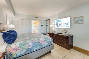 Un dormitorio con cama, cómoda, televisor y puerta que da a un baño.