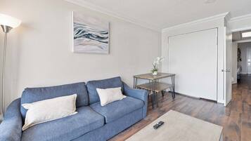 A living room with a blue sofa, a small table, a remote control, and a door leading to another room.