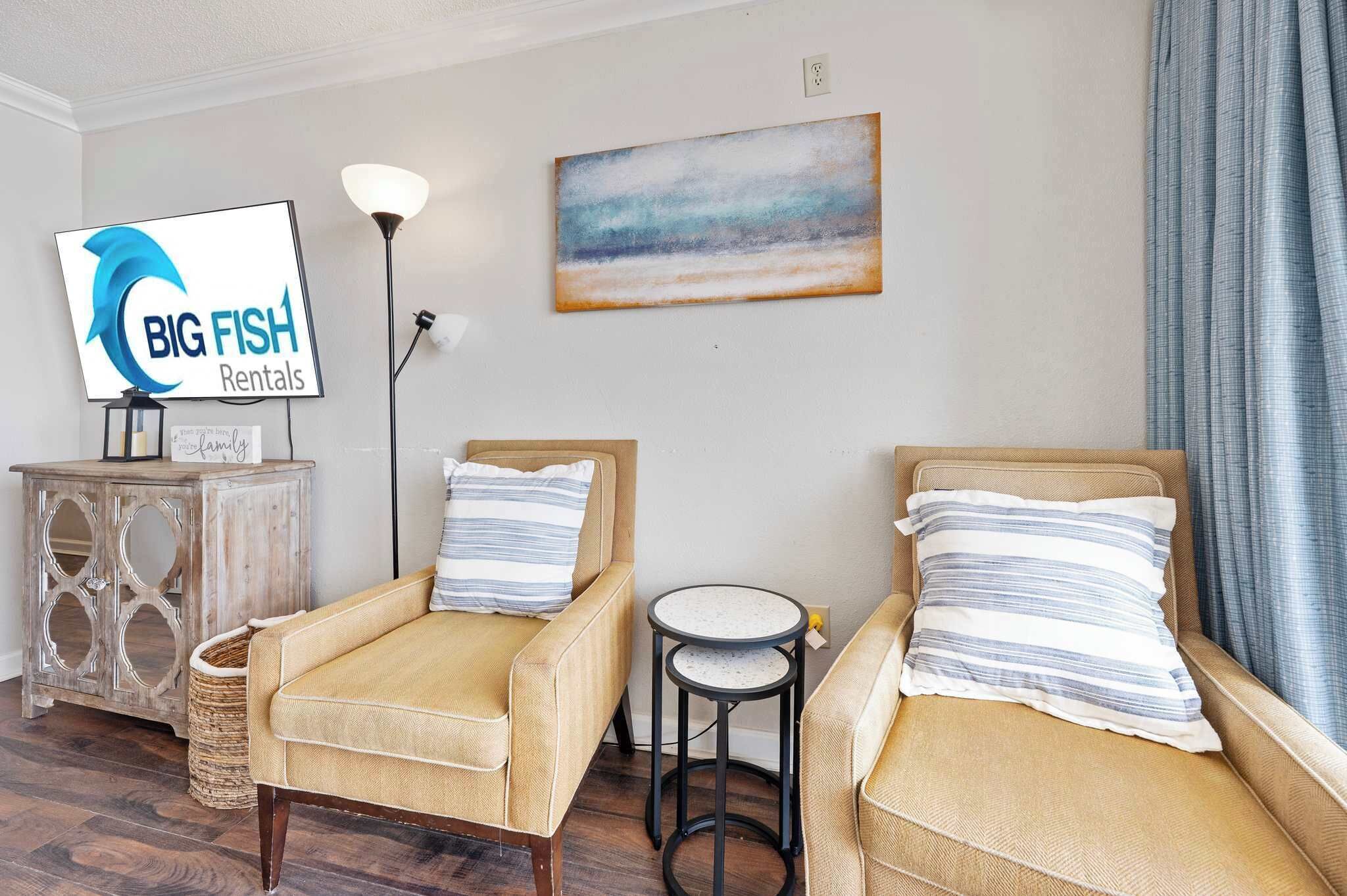 Quarto mobiliado com dois sofás, uma mesinha redonda, um abajur, um quadro e uma TV exibindo 'BIG FISH Rentals'.