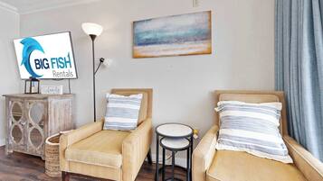 Quarto mobiliado com dois sofás, uma mesinha redonda, um abajur, um quadro e uma TV exibindo 'BIG FISH Rentals'.