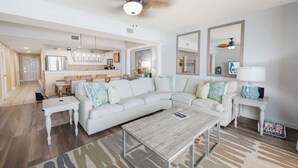 A modern living room with a white sectional sofa, a coffee table, and a dining area with wooden chairs. - Ocean-view condo with balcony & beach access (Myrtle Beach)
