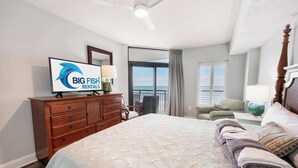 A bedroom with a bed, a dresser, a television, a chair, a window with a view, and a balcony. - Ocean-view condo with balcony & beach access (Myrtle Beach)